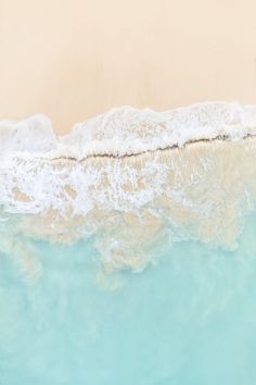 the water is clear and blue with waves coming in from the shore line, as seen from above