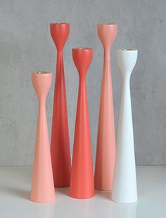 four different colored vases sitting next to each other on a white counter top in front of a concrete wall