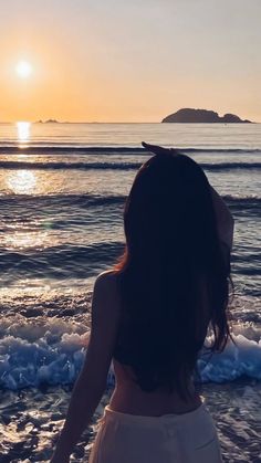 a woman standing on top of a sandy beach next to the ocean at sunset or sunrise