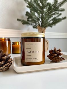 a jar of frasier fir sits on a tray next to pine cones and candles