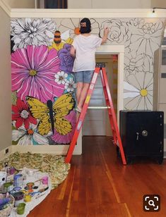 a person on a ladder painting a flowered wall with flowers and butterflies in the background