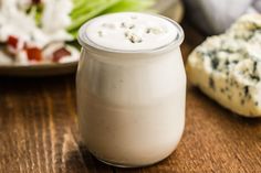 a glass jar filled with white liquid sitting on top of a wooden table next to a plate of food