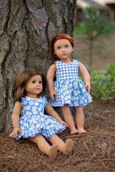 two dolls are sitting next to a tree