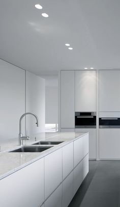 an empty kitchen with white cabinets and counter tops, along with stainless steel sink faucets