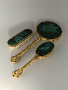 three green and gold hair brushes sitting next to each other on top of a white surface