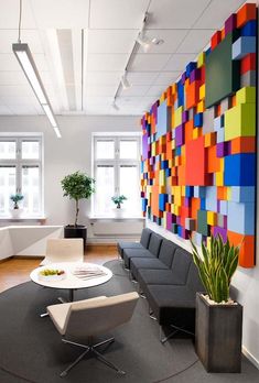 an office with colorful art on the wall and chairs in front of it, along with potted plants