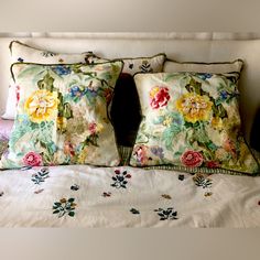 two pillows on top of a bed with white sheets and floral print pillowcases