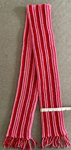 a red and white striped scarf laying on top of a gray table next to a measuring tape