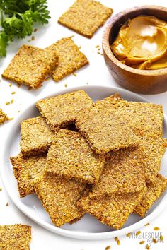 some crackers are on a plate next to a bowl of peanut butter and parsley