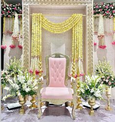 a pink chair sitting in front of a white and gold stage with flowers on it