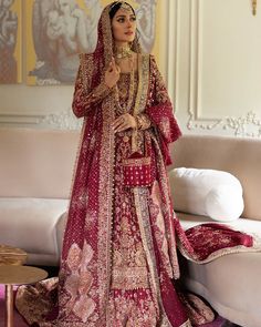 a woman in a red and gold bridal gown standing on a couch with her hands behind her head