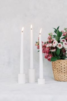 three white candles sitting next to each other with flowers in front of them on a table