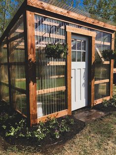 a small greenhouse with glass doors and plants growing in the ground next to it's door