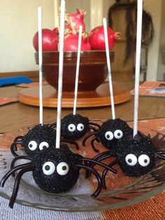 black spider cake pops on a glass plate with white sticks sticking out of it's eyes