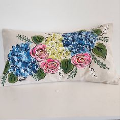 a white pillow with blue and pink flowers on it sitting on a table next to a wall