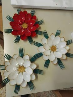 three red and white flowers are sitting on a table with green leaves attached to them