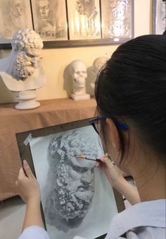 a woman is drawing a busture on a piece of paper in front of some statues