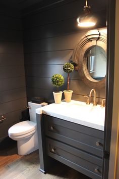 a white toilet sitting next to a sink in a bathroom under a round mirror on the wall