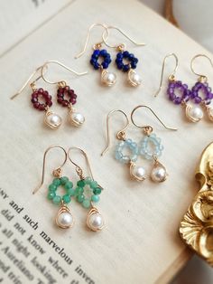 six pairs of earrings sitting on top of an open book with pearls and beads hanging from them