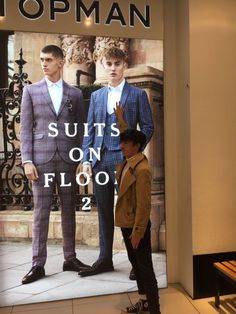 two men standing in front of a store window with the words suits on floor 2