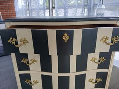 a black and white striped dresser with gold hardware on the top, in front of a window