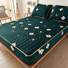 a green bed with white flowers on it in a room next to a chair and table