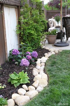 a garden with flowers and rocks in the grass next to a patio area that has an umbrella over it