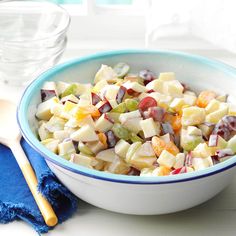 a bowl full of chopped fruit next to a wooden spoon and glass on a table