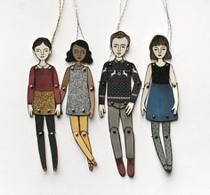 three paper dolls hanging from chains on a white surface, one is wearing a sweater and the other has leggings