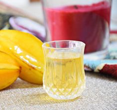 a glass filled with yellow liquid next to some bananas and other fruit on the table