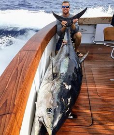 a man sitting on the back of a boat holding up a fish with it's mouth open