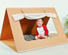 a little boy sitting in a cardboard tent