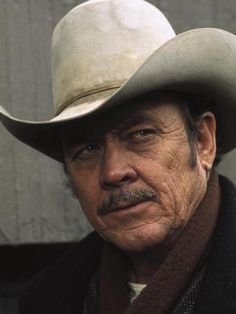 an old man wearing a cowboy hat and scarf looking off into the distance with his hand on his hip