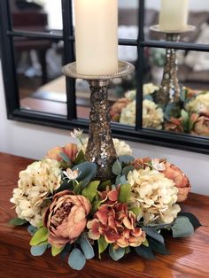 a candle sits on top of a table with flowers in front of a mirror behind it