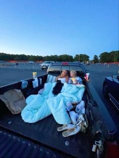 two women laying in the back of a pick - up truck with blankets on it