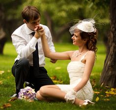 a bride and groom sitting on the grass in front of trees with their hands together