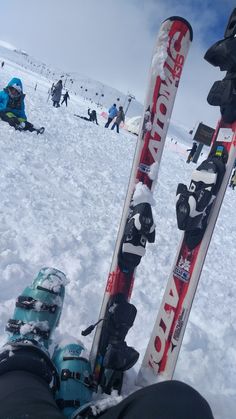 the skis and snowboards are propped up in the snow with people walking around