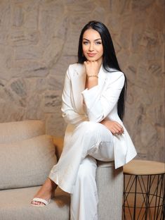 a woman in a white suit is sitting on a chair and posing for the camera