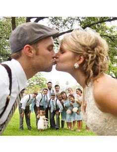 a bride and groom kissing in front of a group of other people on the grass