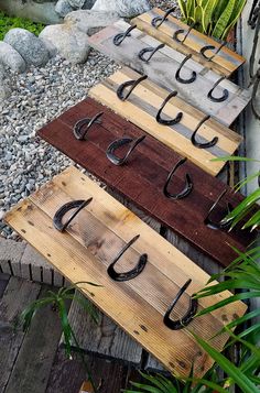 three wooden boards with hooks on them sitting in front of some rocks and plants next to each other