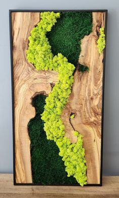 a wood panel with moss and trees in the center on a wooden table next to a gray wall