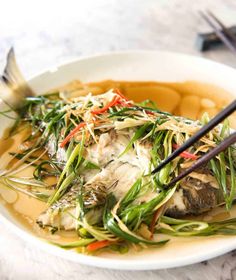 a white plate topped with fish covered in sauce and vegtables next to chopsticks