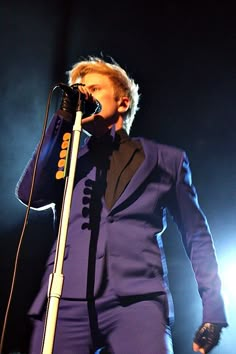 a man in a purple suit singing into a microphone with his hand on the mic