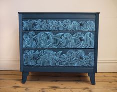 a blue dresser with waves painted on the front and sides, sitting on a wooden floor