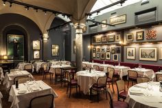 a dining room with tables and chairs covered in white tablecloths, framed pictures on the wall