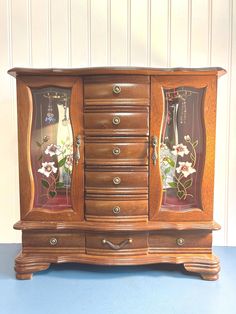 an old wooden cabinet with glass doors and flowers on the front, sitting against a wall