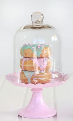 a pink cake stand with donuts under a glass dome