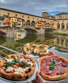 two pizzas sitting on plates in front of a river