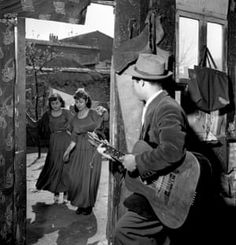 black and white photograph of man playing guitar in front of two women standing outside an old building