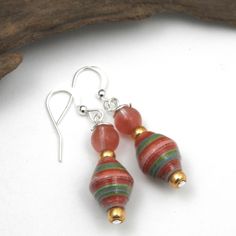 two red, green and gold beaded earrings sitting on top of a piece of wood